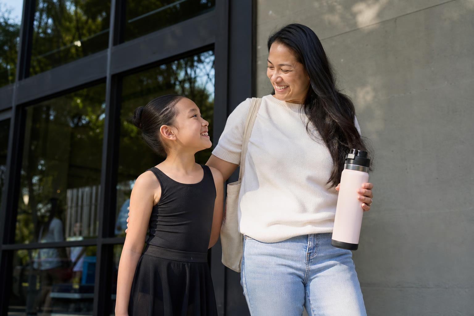 Parent holding a reusable water bottle outside a dance recital venue with a child in dance clothes