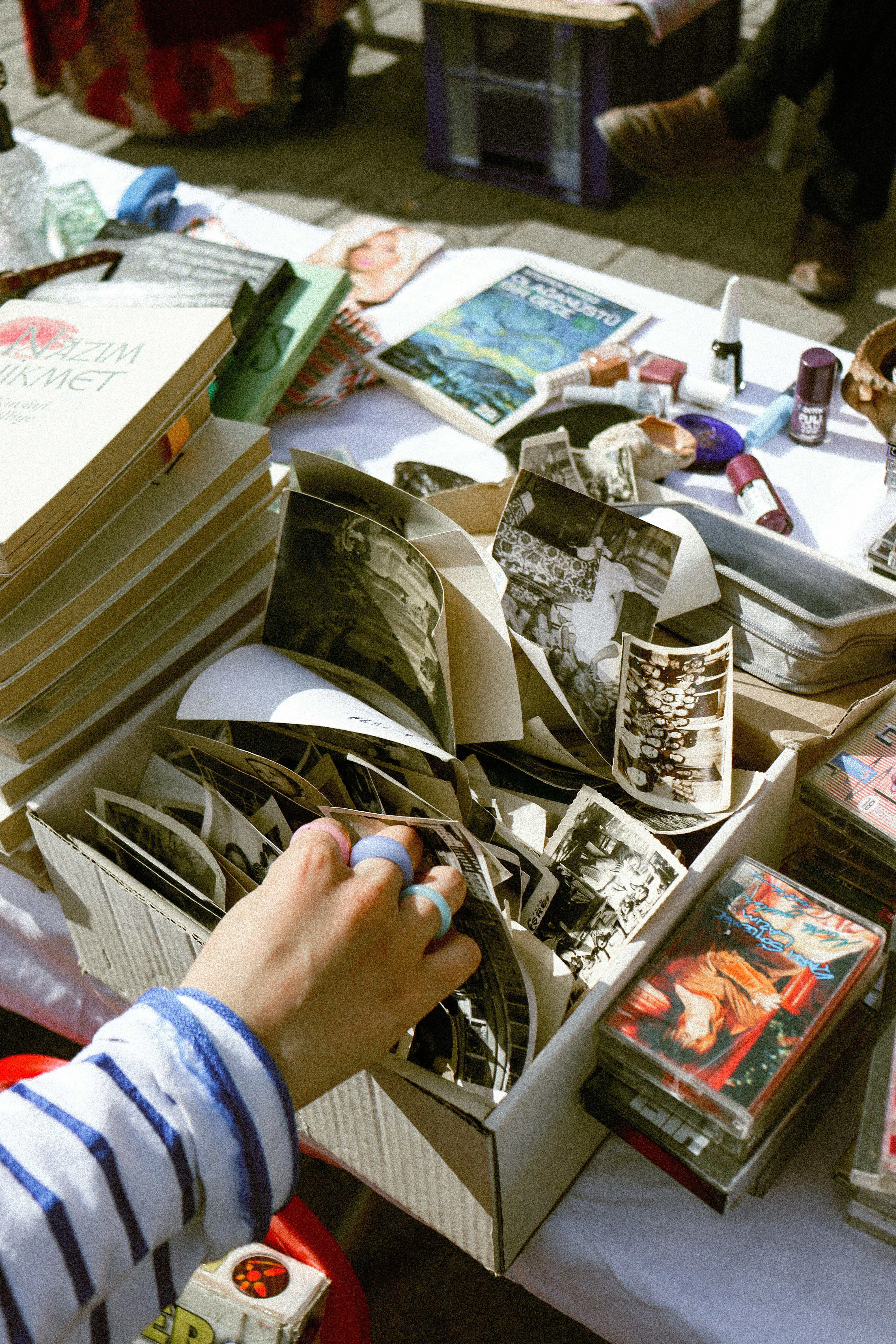 Person browsing through old photos and small vintage finds at a flea market table during a sunny outdoor market day